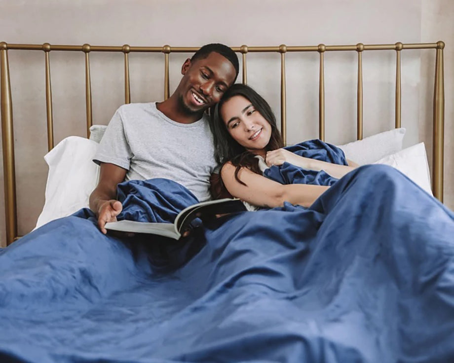 a couple reading a book together in bed under a blue weighted blanket