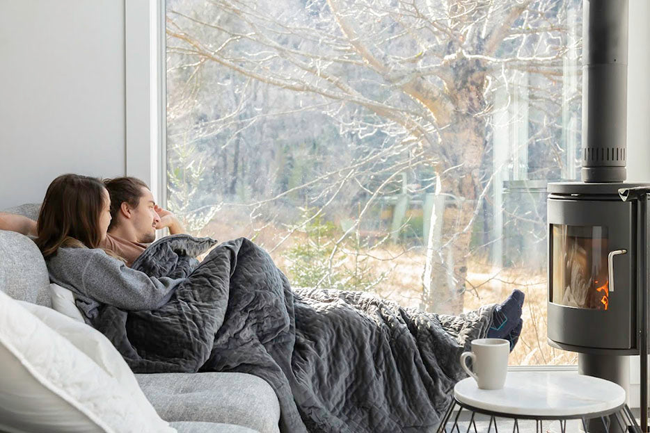 a couple sitting together on a couch under a weighted blanket
