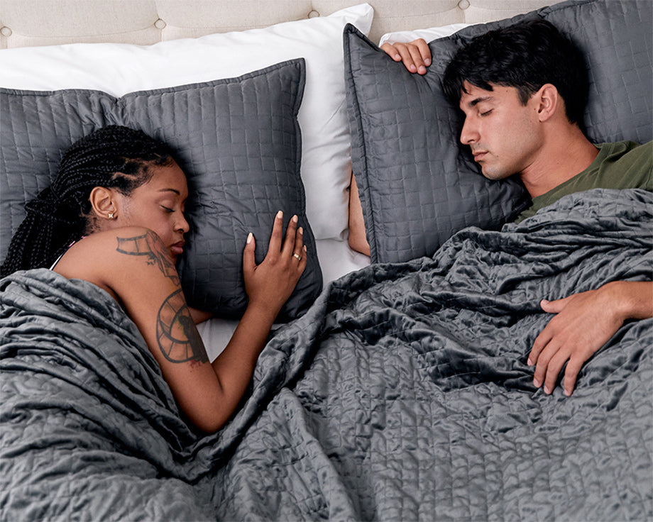 a couple sleeping under a grey weighted blanket
