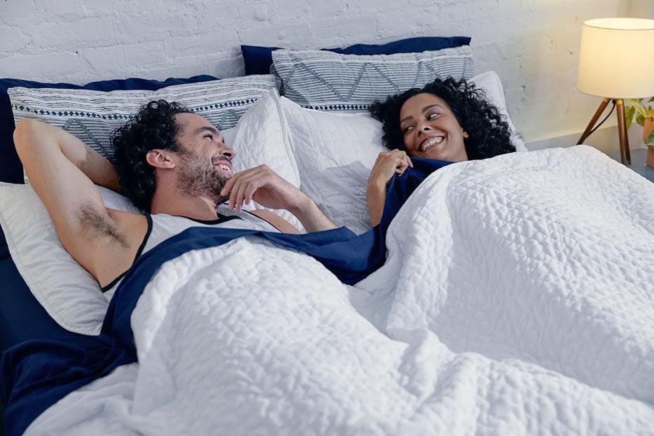 a couple talking while laying under a white weighted blanket