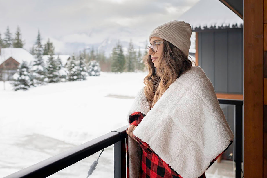 a woman wrapped in a plaid weighted blanket looking out at the snow from her porch