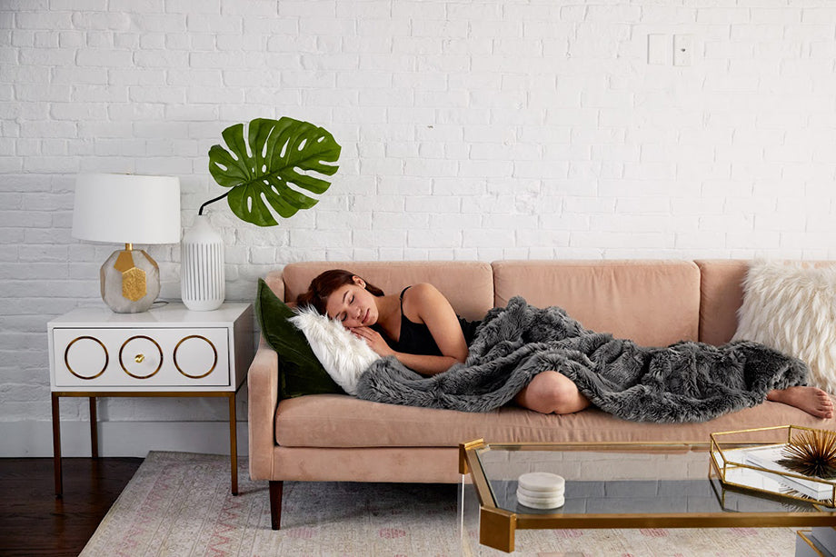a woman sleeping on a couch under a gray weighted blanket