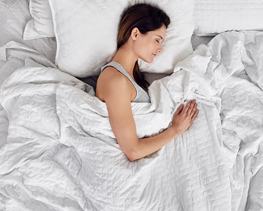 a woman sleeping under a white weighted blanket