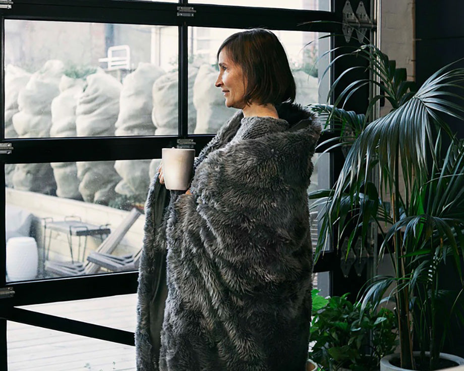 a woman wrapped in a grey weighted blanket holding a mug