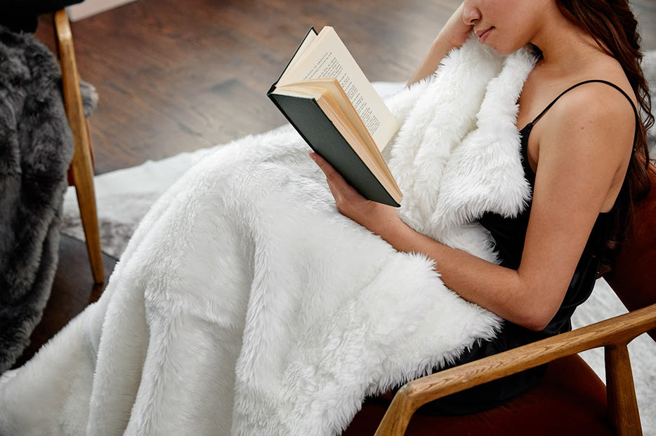 a woman sitting in a chair reading a book wrapped in a weighted blanket