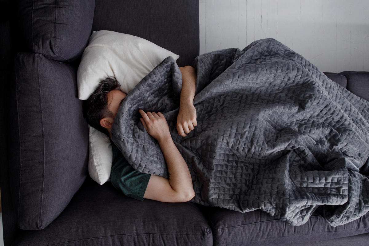 man lying on couch covered by a grey Gravity weighted blanket