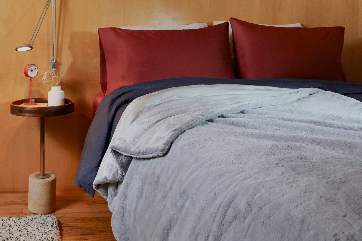 Grey faux rabbit fur weighted blanket laid on top of a bed