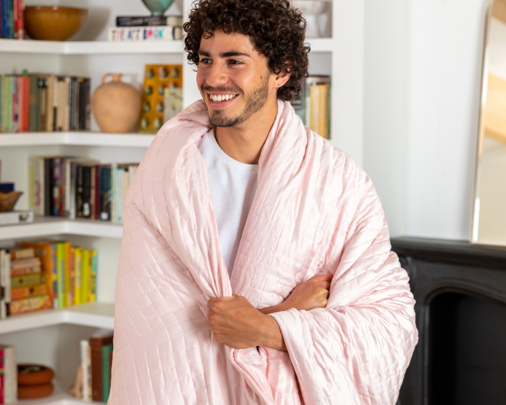 A smiling man wrapped in a Dusty Pink Gravity Weighted Cooling Blanket - #color_dusty-pink