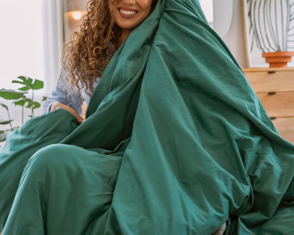 Young woman smiling and wrapped in a Forest Green Basics by Gravity Cotton Duvet Covers  - #color_forest-green