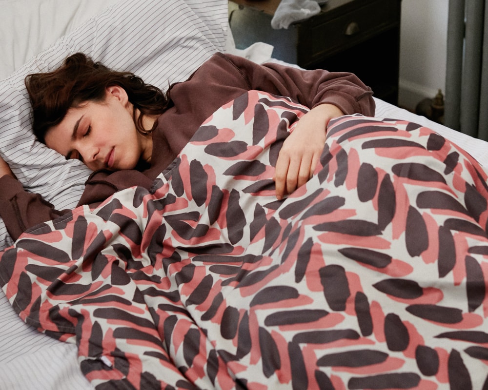 Woman sleeping in bed covered by a pink and brown weighted blanket