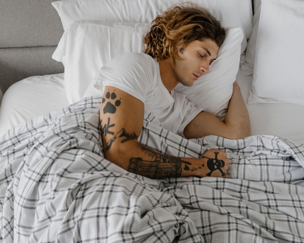 Man asleep on a bed covered by a grey flannel weighted blanket #color_grey-plaid