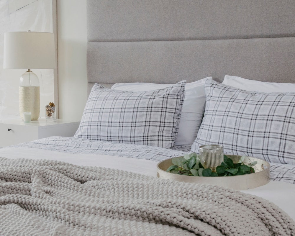 Made bed with grey flannel contemporary bedding and a circular tray with eucalyptus sitting on the surface #color_grey-plaid