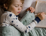 Sleeping young boy holding a book while covered by a gravity green kids blanket