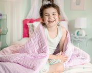 Smiling young girl sitting on a bed with a light pink kids gravity blanket