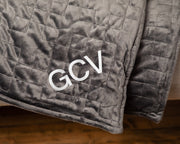 Closeup of the corner of a grey gravity weighted blanket draped with the initials GCV