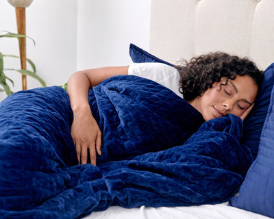Woman sleeping in bed while covered by a navy blanket - #color_navy