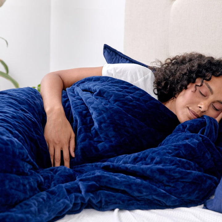 Woman sleeping in bed while covered by a navy blanket - #color_navy